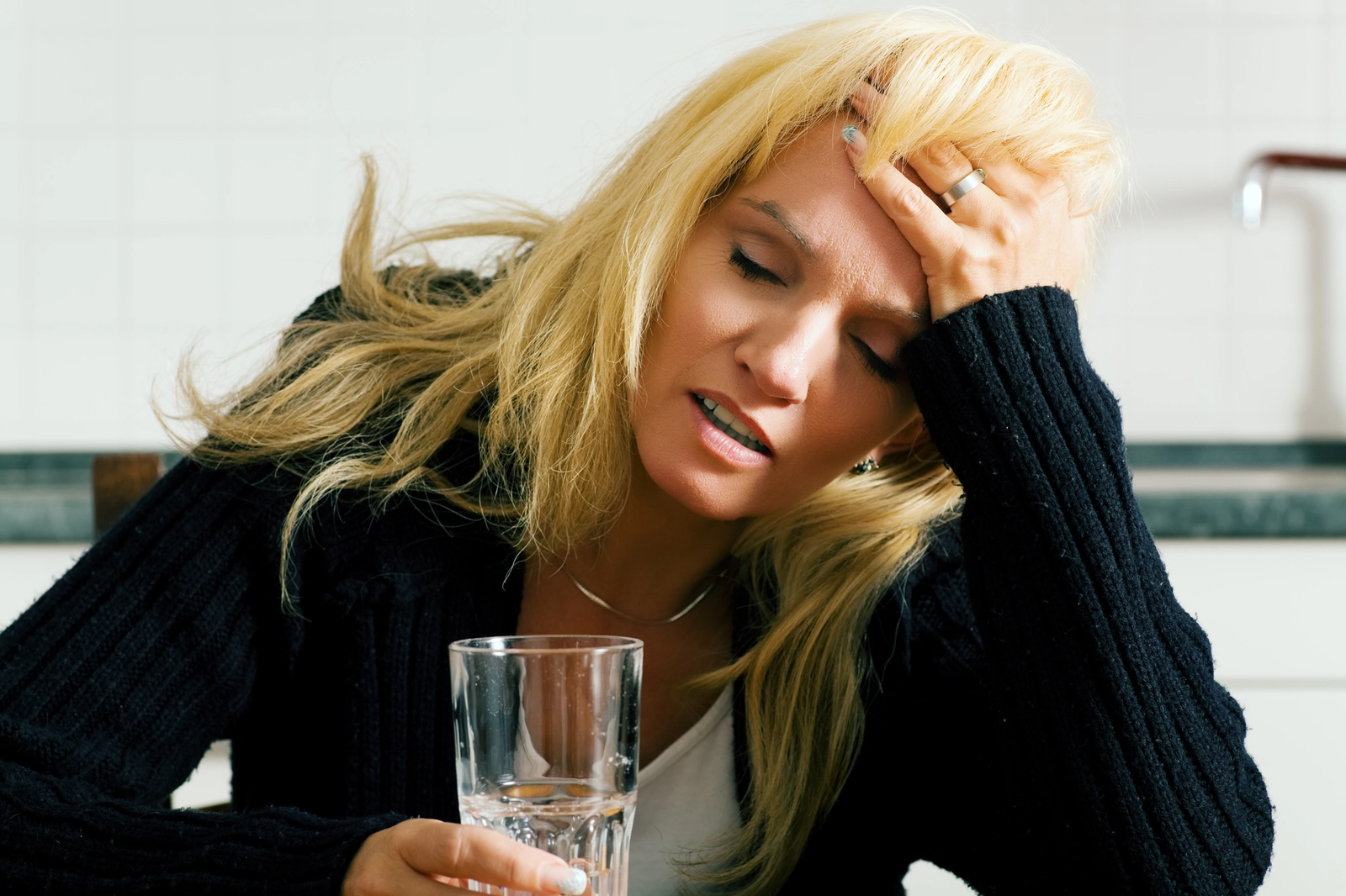 a hungover person holds a glass of water in one hand while cupping their forehead with the other