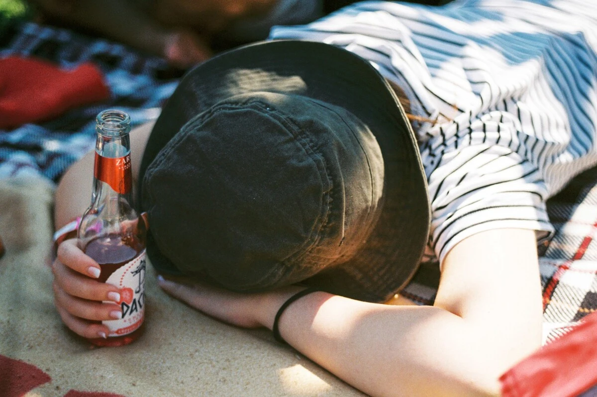 Man with alcohol gastritis laying his head on his arm and holding a half empty bottle of beer in one hand.