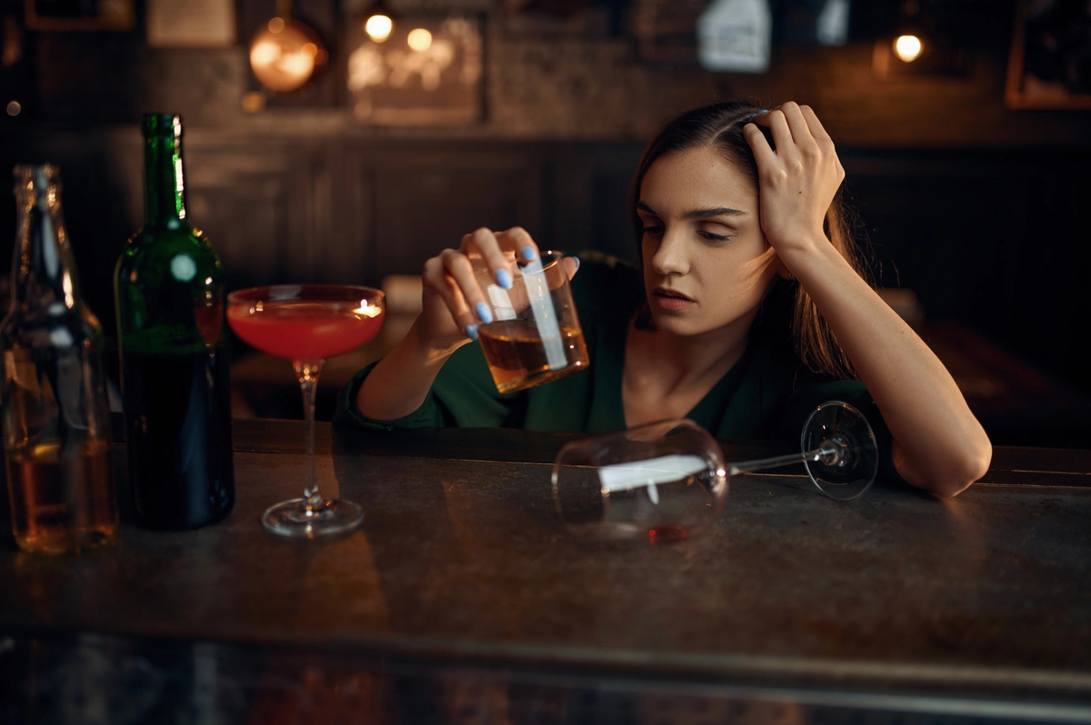 Woman with alcohol gastritis drinking in excess at a bar surrounded by multiple alcoholic drinks