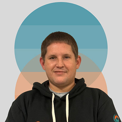 Person wearing a black hoodie and smiling in front of geometric background.